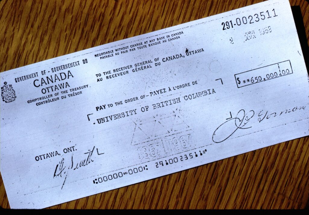 A simple cheque, totalling $650,000 and addressed to the University of British Columbia and from the Comptroller of the Treasury of the Government of Canada. The white cheque sits on a wood grain surface.